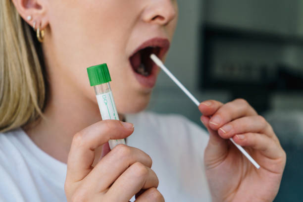 Wanita muda memegang swab ke mulutnya dan memegang tabung medis untuk tes rumah virus corona / covid19