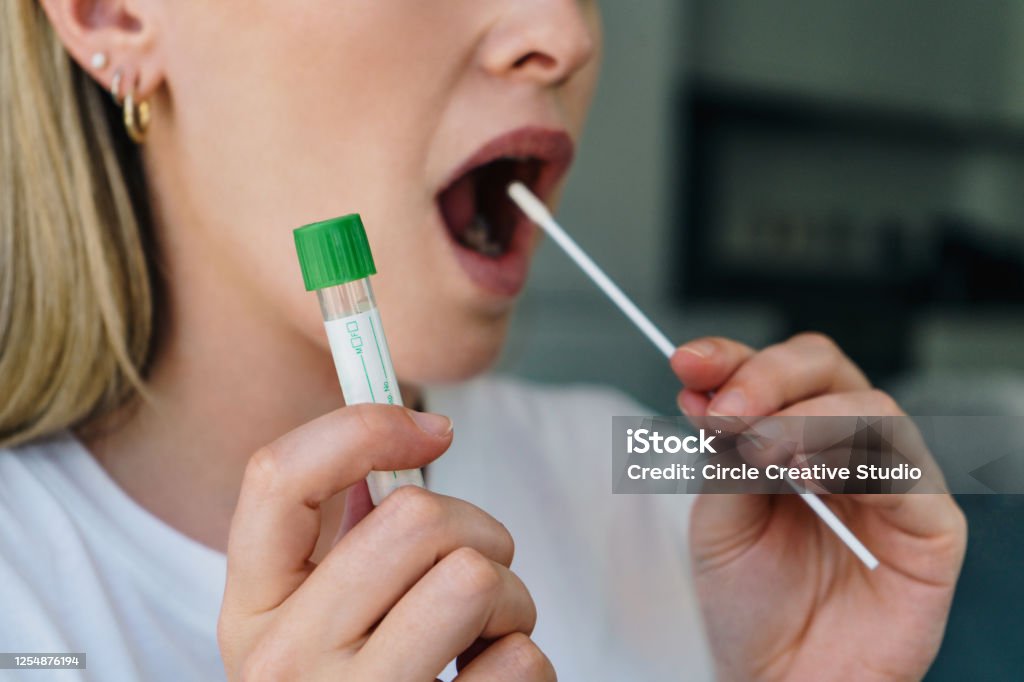 Coronavirus Home Test (COVID-19) Young woman  holds a swab into her mouth and holding a medical tube for the coronavirus / covid19 home test Coronavirus Stock Photo