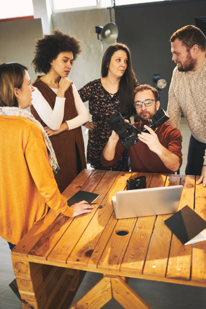istock Young handsome bearded educator showing to his multicultural attendees how camera works. Photo studio interior. 1254876417