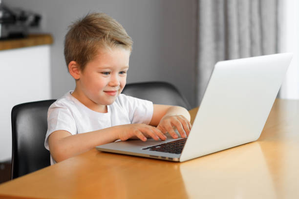 istock Funny young boy using a laptop computer sitting on top of a table at home 1254877134