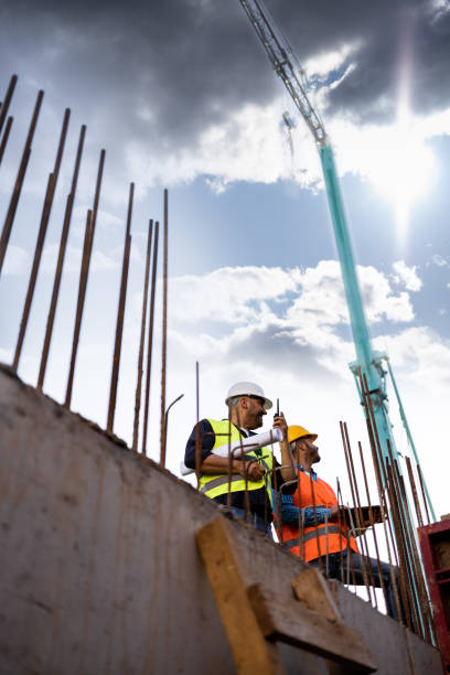 istock Men in hardhat and yellow and orange jacket posing on building site 1254878734