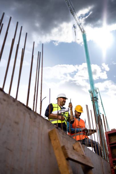 istock Men in hardhat and yellow and orange jacket posing on building site 1254878741