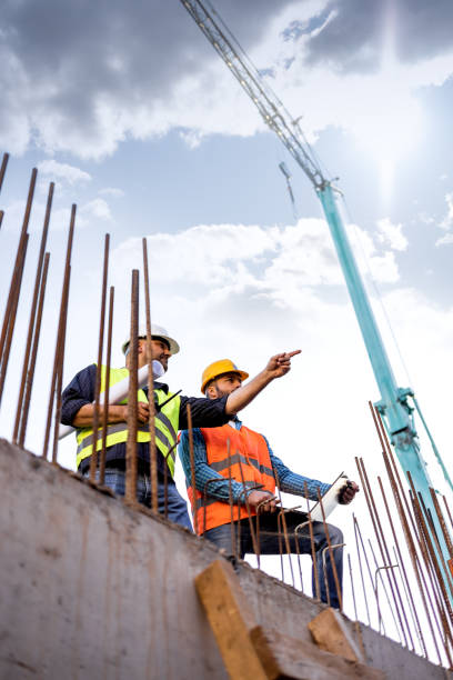 istock Men in hardhat and yellow and orange jacket posing on building site 1254878805