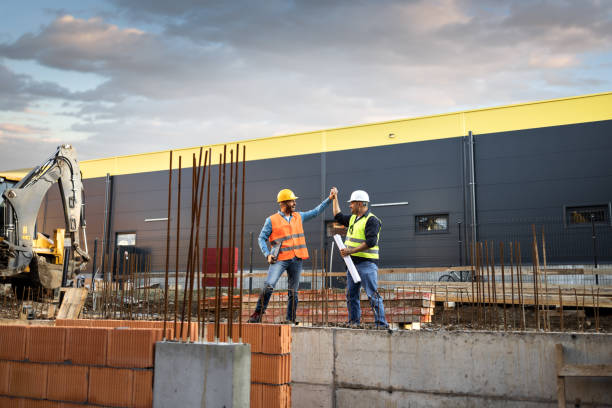 istock Men in hardhat and yellow and orange jacket posing on building site 1254879103