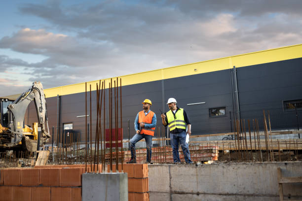 istock Men in hardhat and yellow and orange jacket posing on building site 1254879643
