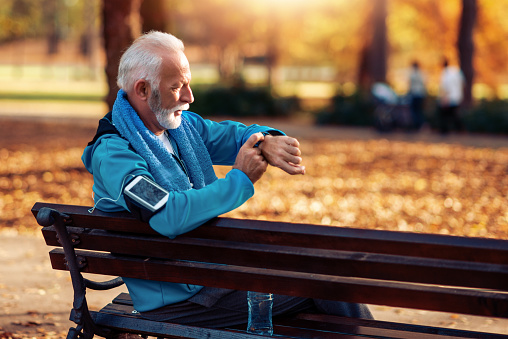 Senior athlete man resting on bench in park at sunset after running.