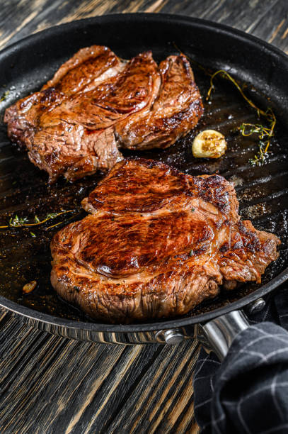istock Cooked grilled marble steak Chuck roll in a pan. Dark background. Top view 1254888637