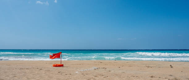 istock Red flag waving in the wind on a beach 1254889025