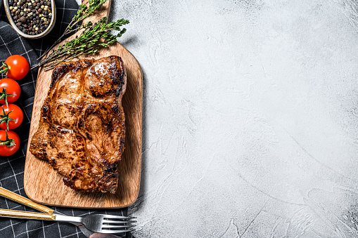 Pork cutlet steak on the bone with spices and herbs. Gray background. Top view. Copy space.