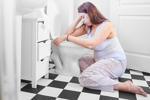 A woman is knelt at the toilet with her head in her hands over the toilet bowl as she struggles with her morning sickness