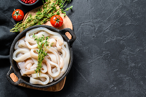 Fresh raw squid rings in a steel bowl. Black background. Top view. Copy space.
