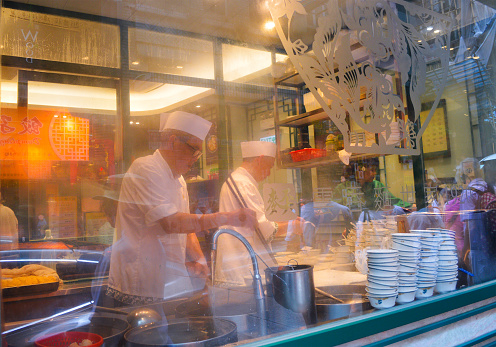 Hong Kong, August 2018. A street-facing window shows chefs cooking inside the famous Hong Kong wonton noodle restaurant \