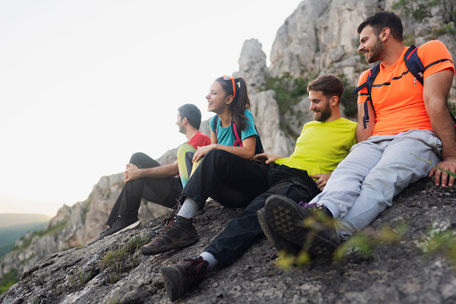 Young group of hikers relaxing on the top of a mountain and enjoying the view. They watch the sunset with a smile.