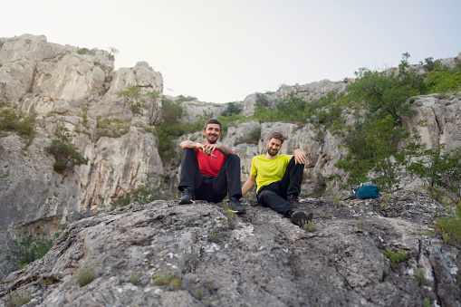 Two Caucasian young men relaxing on the top of a mountain. Smiling and enjoying the view.