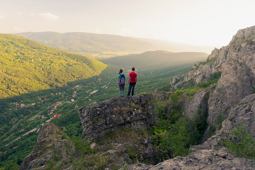 Young Caucasian man and woman standing on the edge of a cliff looking at the valley.