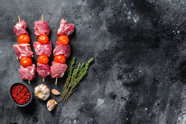 istock Raw beef meat kebab. BBQ with tomato and spices.  Black background. Top view. Copy space 1254897683