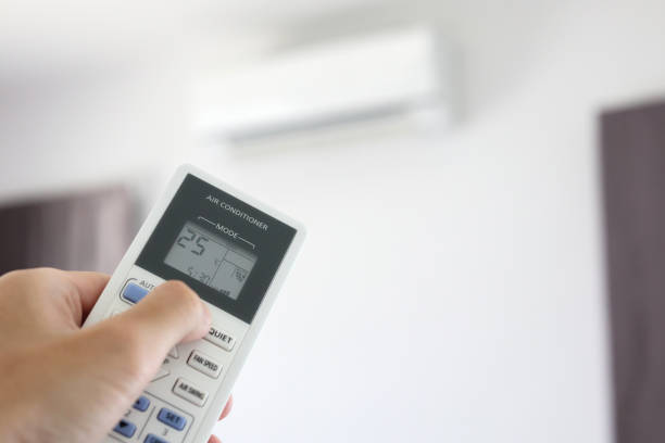 istock Hand with remote control directed on air conditioner inside the room 1254898171