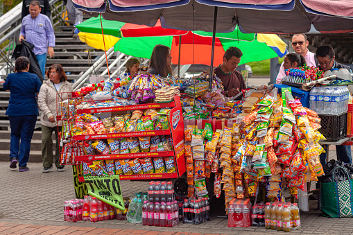 Bogotá, Colombia - May 17, 2017: Roadside vendors sell snacks and drinks to people coming from or going to a Transmilenio Bus Rapid Transit station where Calle 125 meets the Auropista Norte in the Andean capital city. A variety of snacks and drinks can be seen. Image shot in the early afternoon sunlight on an overcast day. Focus on packets.