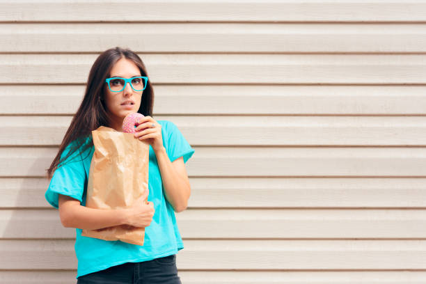 lustige mädchen essen donuts straße aus einer papiertüte - bulimia stock-fotos und bilder