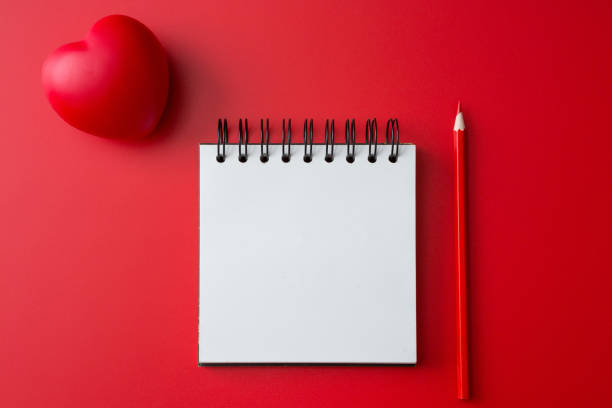 istock Top view of Notebook, pencil, heart shaped ball on a red background and copy space 1254920113