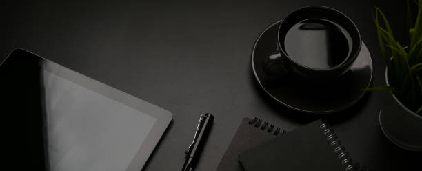 istock Dark office desk with digital tablet, stationery, pen, coffee cup and copy space 1254924178