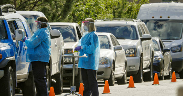 Two Female Nurses Wearing Gowns, Surgical Face Masks, Gloves, and Face Shields Talk to Patients in their Cars in a Drive-Up (Drive Through) COVID-19 (Coronavirus) Testing Line Outside a Medical Clinic/Hospital Outdoors (Second Wave) Two Female Nurses Wearing Gowns, Surgical Face Masks, Gloves, and Face Shields Talk to Patients in their Cars in a Drive-Up (Drive Through) COVID-19 (Coronavirus) Testing Line Outside a Medical Clinic/Hospital Outdoors (Second Wave) frontline worker mask stock pictures, royalty-free photos & images