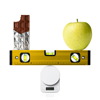 Construction bubble level with chocolate and green apple, on the kitchen digital food weight scale, isolated on white background.
Diet concepts.