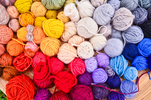 Flat lay picture of many colorful and bright ravels of wool, laying in a large wooden bowl standing on the ground of green grass