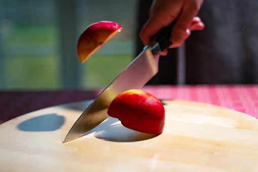 Close up of chef hand chopping apple in half with kitchen knife on the table. Slicing red apple on wooden board