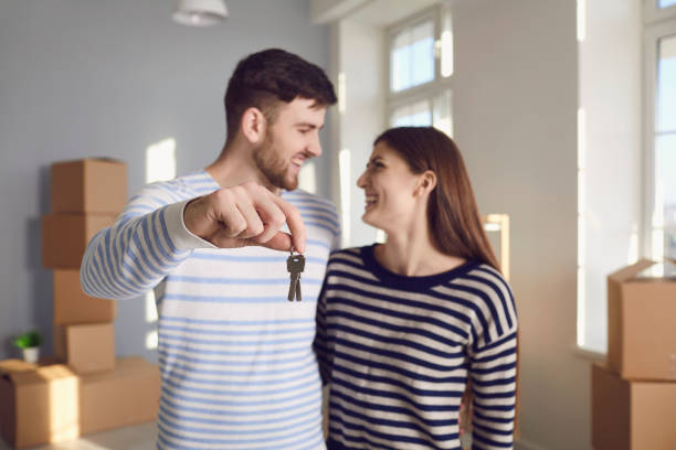 couples heureux avec des clefs à la nouvelle maison dans les mains souriant tout en restant dans la pièce. - apartment contemporary action packing photos et images de collection