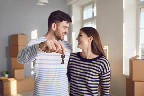 部屋に立っている間に微笑んで手で新しい家への鍵を持つ幸せなカップル。 - apartment contemporary action packing ストックフォトと画像