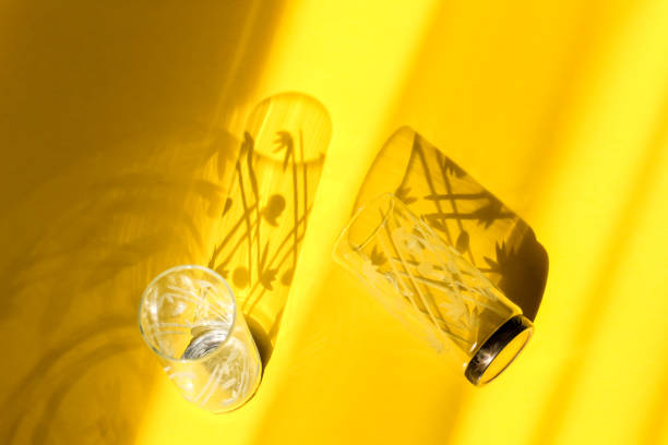 istock Empty glass glasses with floral pattern isolated on a bright yellow background with shadows and sunlight. Abstract, summer, party, celebration, restaurant background. 1254949617