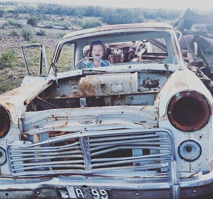 A young boy playing in a old wreck of a car. The car is very rusty and not in a working condition.