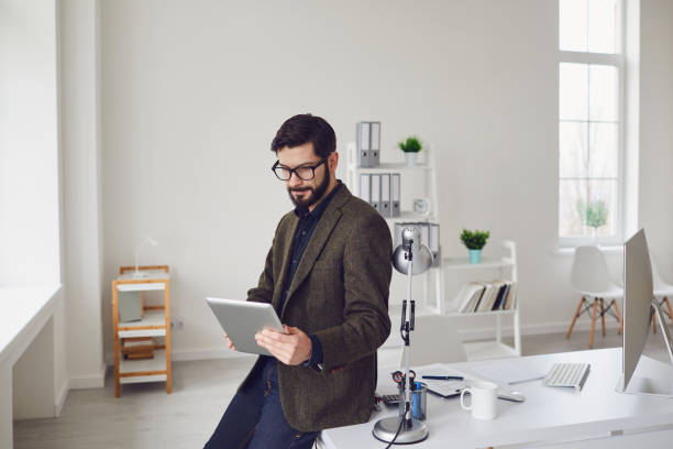 istock Businessman worker with a beard looks at the tablet while standing in the office. 1254953478