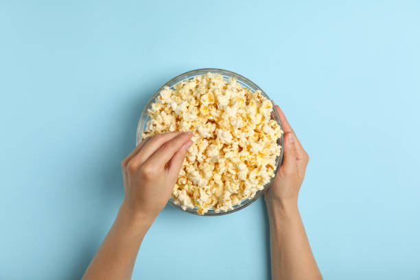istock Male hands and bowl with popcorn on blue background 1254957510