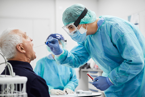 Doctor taking throat swab test from male patient. Medical worker is in protective workwear. They are at hospital during epidemic.