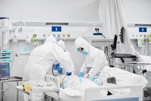 Frontline Workers Treating Male Patient in ICU Frontline workers treating male patient in ICU. Team of doctors are wearing white coveralls. They are in hospital during COVID-19. intensive care unit photos stock pictures, royalty-free photos & images