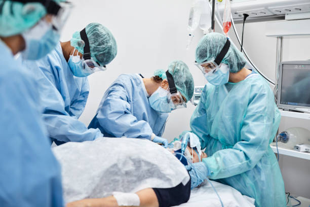 Team of Doctors and Nurses Operating Male Patient Team of doctors and nurses operating male patient in ICU. Frontline workers are treating man for coronavirus. They are in protective workwear. operating room photos stock pictures, royalty-free photos & images