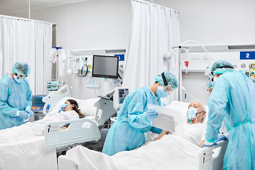 Doctors and nurses taking care of patients in ICU. Team of frontline coworkers are treating man and woman. They are at hospital during COVID-19.