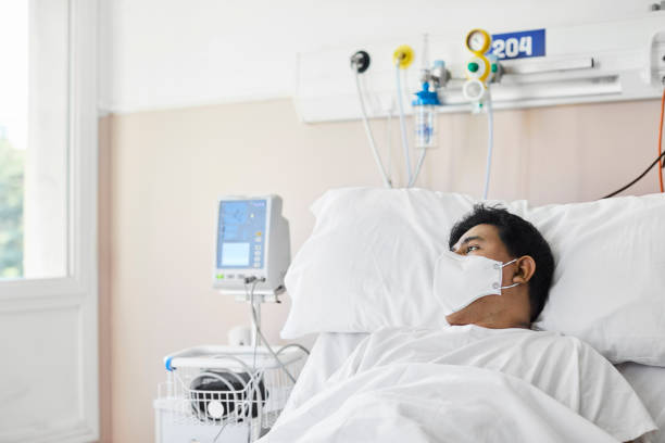 Male Patient Looking Away While Relaxing On Bed Male coronavirus patient looking away while relaxing on hospital bed. Man is wearing protective face mask. He is in hospital during pandemic. person wearing n95 mask stock pictures, royalty-free photos & images