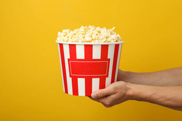 istock Male hands holding bucket with popcorn on yellow background 1254958741