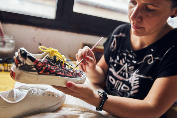 istock Focused creative female artist applying a waterproof paint on sneakers 1254962938
