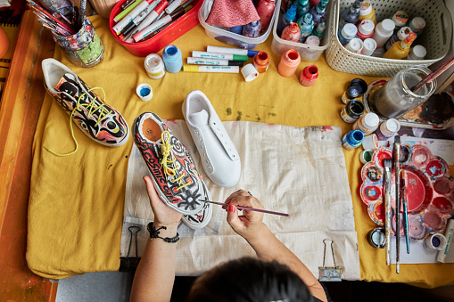 Mid adult female alternative artist painitng on a sneakers in her messy workshop at balcony