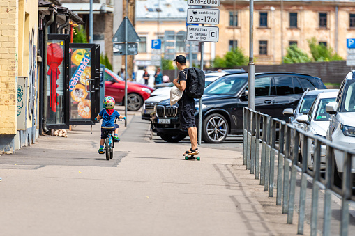 Riga, Latvia- July 3, 2020: a man with a skateboard and a child with a bicycle on the sidewalk in the city, ecological mode of transport