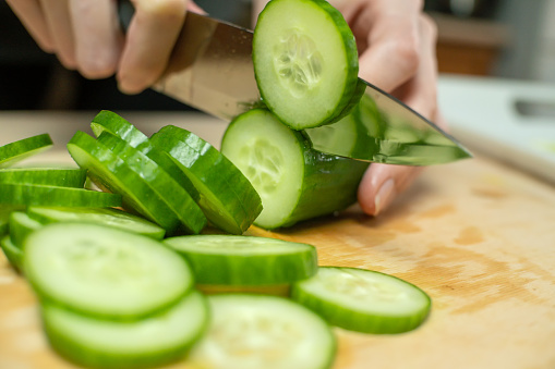 Women's hands cut a fresh cucumber into circles on a wooden Board close up