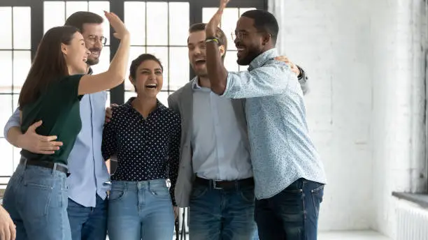 Photo of Multiethnic employees accomplish project celebrating success giving high five