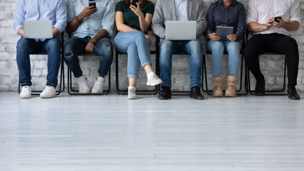 istock Six multiethnic young people sit in queue holding electronic devices 1254975591