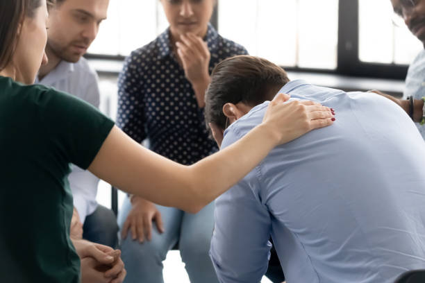 During group therapy session participants supporting crying desperate guy During group therapy session participants supporting crying desperate guy, provide psychological assistance talking encouraging words share mental pain try to help, struggle with addictions treatment hopelessness stock pictures, royalty-free photos & images