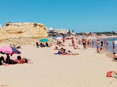 Scene Of Restaurant, Rock Formation, Building Exterior, People Standing, Looking Around, Swimming, Sunbathing, Sitting Down At Portimao Beach In Faro Algarve Portugal Europe