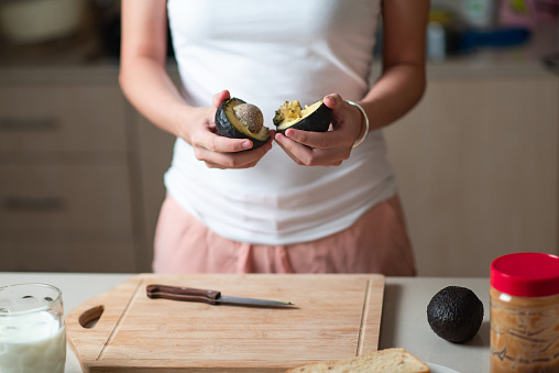 Woman cutting avocado for making a sandwich with peanut butter at home closeup